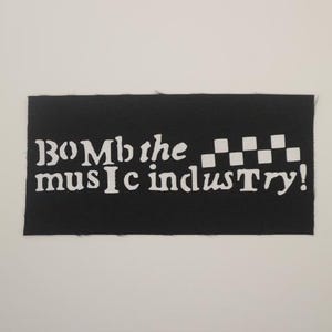 May include: Black fabric patch with white text that reads "Bomb the music industry!" with a checkered pattern to the right of the text.
