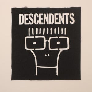 May include: Black and white patch with the word "DESCENDENTS" in white lettering. A cartoon character with glasses and a simple body is below the text.