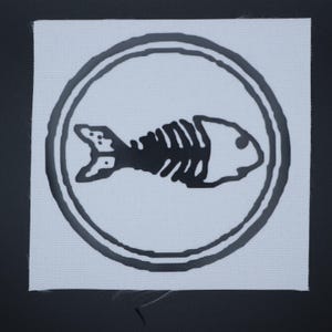 May include: Square white patch with a black circular border. Inside the circle is a black fish skeleton design. The patch is on a black background.