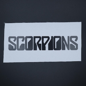 May include: A rectangular patch with the word "SCORPIONS" in a bold, stylized font. The text is in a gradient of gray and black, set against a light gray, textured background. The patch is likely for clothing or accessories.