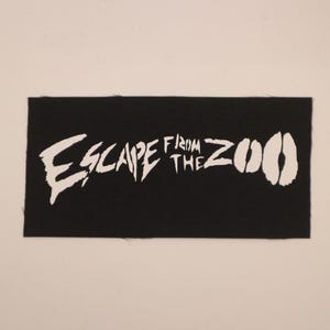 Op de afbeelding: Zwart rechthoekig embleem met de witte tekst "ESCAPE FROM THE ZOO". Het woord "ESCAPE" is in een vet, gekarteld lettertype, en het woord "ZOO" wordt weergegeven door twee witte dierensporen.