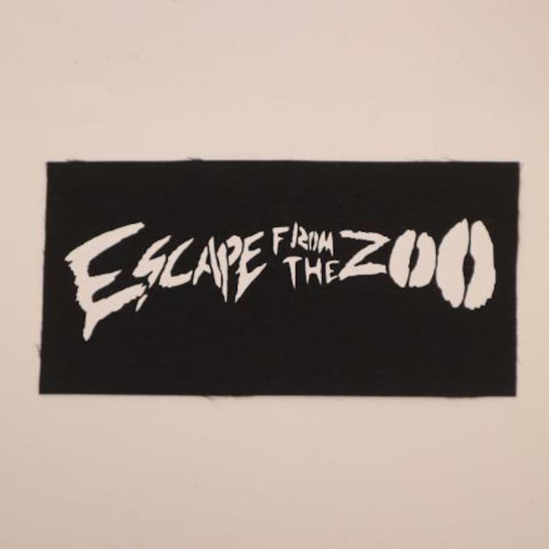 Op de afbeelding: Zwart rechthoekig embleem met de witte tekst "ESCAPE FROM THE ZOO". Het woord "ESCAPE" is in een vet, gekarteld lettertype, en het woord "ZOO" wordt weergegeven door twee witte dierensporen.