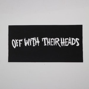May include: Black rectangular patch with the text "OFF WITH THEIR HEADS" in white, stylized lettering. The patch has a ribbed texture and is set against a white background. The text is the primary focus.
