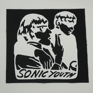May include: Black and white patch featuring a graphic of two figures with the text "SONIC YOUTH". The figures are in profile, with one raising two fingers. The patch is square and has a black background.