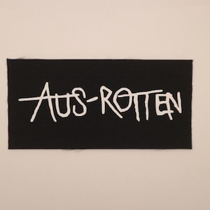 May include: A black rectangular patch with the white text "AUS-ROTTEN" in a handwritten style. The patch has a textured surface and is set against a neutral background.