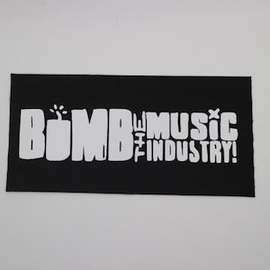 May include: Black rectangular patch with white text that reads "BOMB THE MUSIC INDUSTRY!" The word "BOMB" is stylized with a bomb graphic. The patch has a ribbed texture.