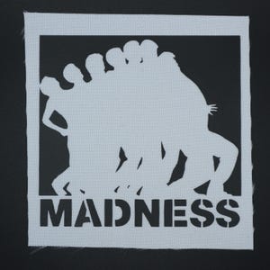 May include: A white rectangular patch with a black border features a white silhouette of several figures in motion. The word "MADNESS" is printed in bold, black, stencil-style letters at the bottom of the patch.