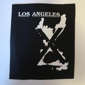 May include: Black patch with the words "LOS ANGELES" in white block letters above a white graphic of the city's outline with a large white "X" superimposed over it. The patch is square.