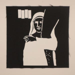 May include: Black and white iron-on patch featuring a nun with a black background and the text "III" in a window behind her.