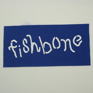 Op de afbeelding: Een rechthoekige blauwe stoffen patch met het woord "fishbone" in witte sjabloonletters. De patch is effen blauw van kleur en de tekst is gecentreerd op de patch.