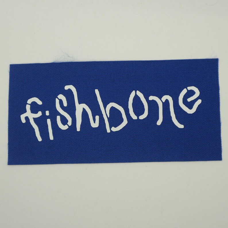 Op de afbeelding: Een rechthoekige blauwe stoffen patch met het woord "fishbone" in witte sjabloonletters. De patch is effen blauw van kleur en de tekst is gecentreerd op de patch.