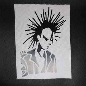 May include: A rectangular white fabric patch featuring a black screen-printed graphic of a person with a tall, spiky mohawk hairstyle. The figure is depicted from the chest up, wearing a collared jacket, with a stylized hand visible on the left side.
