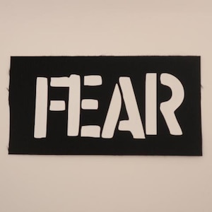 May include: Black fabric patch with the word "FEAR" in white block letters.