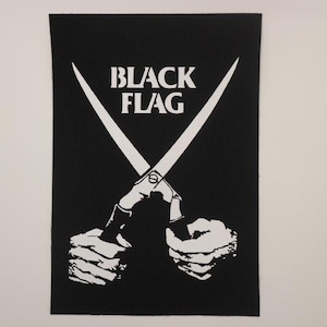May include: Black patch featuring the words "BLACK FLAG" in white block letters above a white illustration of scissors crossed over two white hands. The patch has a black background.