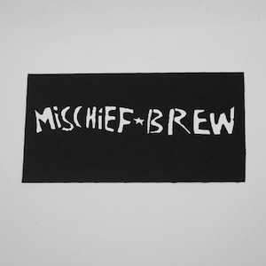 May include: A black rectangular patch with the white text "MISCHIEF * BREW". The text is in a stylized font. The patch is likely made of fabric and is against a white background.