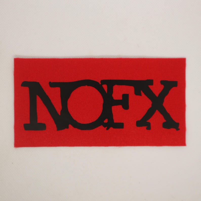 Peut inclure: Un &eacute;cusson rectangulaire rouge avec les lettres noires "NOFX" imprim&eacute;es dessus. Les lettres sont dans une police en gras, l&eacute;g&egrave;rement vieillie. L'&eacute;cusson a un aspect textur&eacute;.