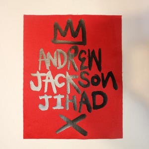 May include: Red fabric patch with black and silver lettering. The text reads "ANDREW JACKSON JIHAD" with a crown above the first name and an X below the last name.