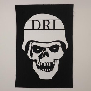 May include: Black and white patch with a skull wearing a helmet. The helmet has the word "DRI" written on it.