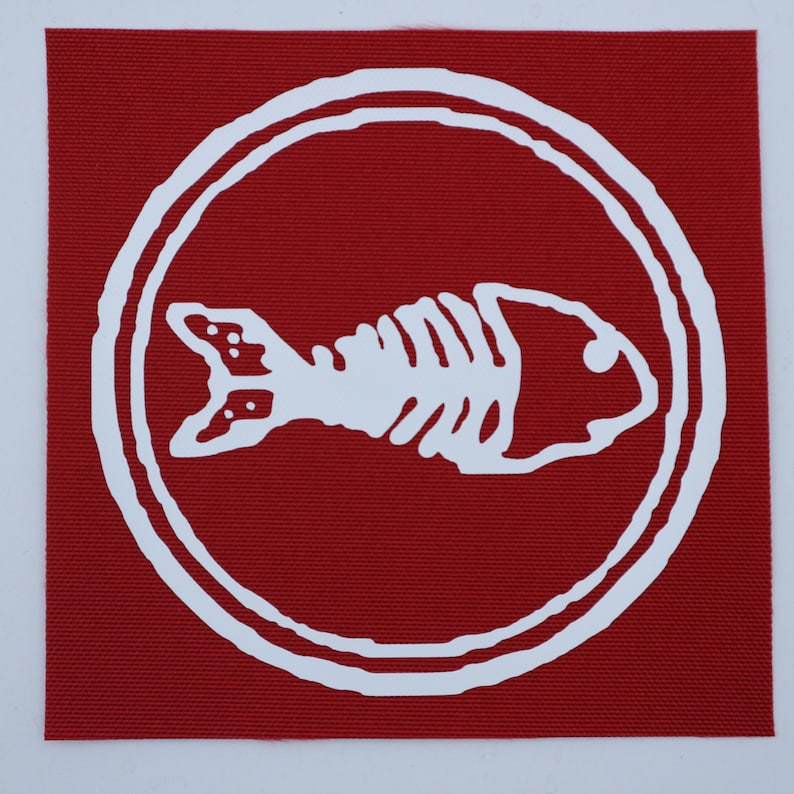 Puede incluir: Un parche cuadrado rojo con un dise&ntilde;o de esqueleto de pez blanco dentro de un borde circular blanco. El esqueleto del pez es una ilustraci&oacute;n detallada y el parche tiene una apariencia texturizada.