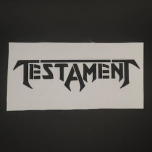 May include: Black and white patch with the word "TESTAMENT" in a stylized font.