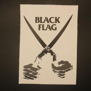 May include: A white rectangular patch featuring the words "BLACK FLAG" in bold, black capital letters. Two black scissors are crossed over each other, with the handles held by two hands.