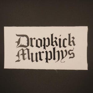 May include: White fabric patch with black lettering that reads "Dropkick Murphys" in a gothic font.