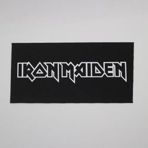 May include: Black rectangular patch with the white text "IRON MAIDEN" in a stylized font. The patch is likely made of fabric and is suitable for sewing or ironing onto clothing or accessories. The design is a popular band logo.
