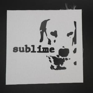 May include: White square fabric with a black graphic of a skull and the word "sublime" in a sans-serif font. The skull design is stylized and partially visible. The fabric has a textured appearance.