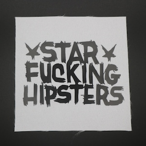 May include: Square white fabric patch with the words "STAR FUCKING HIPSTERS" in bold black letters. The text is arranged in three lines, with star-like symbols on either side of the word "STAR".