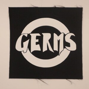 May include: Black fabric patch with a white circle and the word "GERMS" in white letters inside the circle.