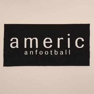 May include: A black rectangular patch with the word "americ" above "anfootball" in white, sans-serif font. The patch has a textured surface and is set against a neutral background. The text is centered on the patch.