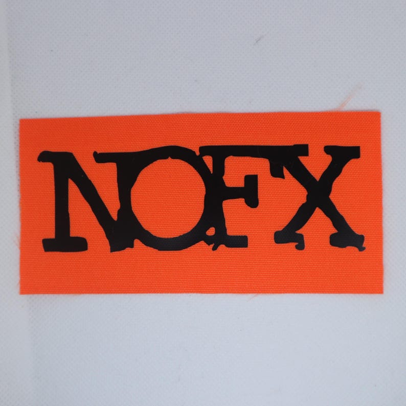 Peut inclure: Un &eacute;cusson rectangulaire orange avec le texte noir "NOFX". Les lettres sont en gras et l&eacute;g&egrave;rement us&eacute;es. L'&eacute;cusson est probablement en tissu et se d&eacute;tache sur un fond blanc.