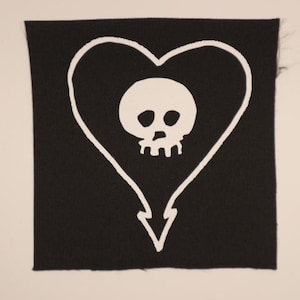 May include: A black square patch featuring a white heart outline with a skull in the center. The heart shape has a downward arrow at the bottom. The skull and heart design is a bold, graphic image.