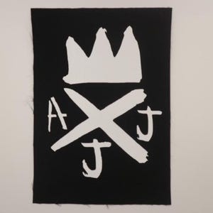 May include: Black and white iron-on patch with a crown and the letters "AJ" crossed over each other.