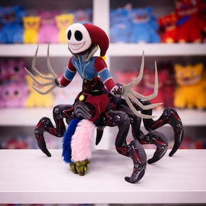 以下が含まれることがあります： ピエロのようなキャラクターがクモのような体に乗り込んだぬいぐるみ。ピエロは白い顔、赤と青の衣装、爪のような腕を持っています。クモの体は黒と赤で、毛皮のようなアクセントがあります。