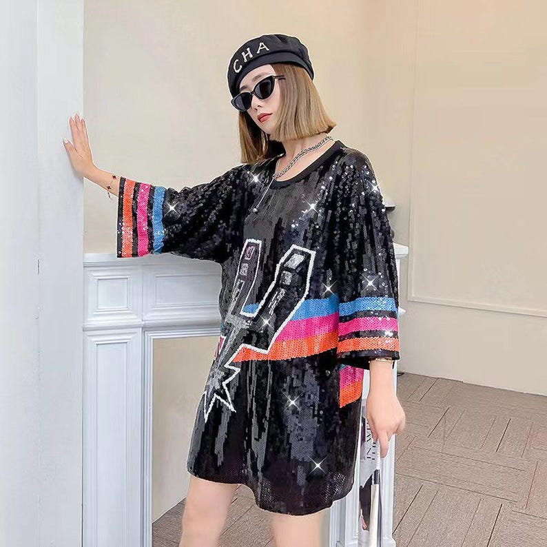May include: Black sequined dress with a lightning bolt design and colorful stripes on the sleeves. The dress has a loose fit and a round neckline. The sleeves are three-quarter length.