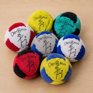 Puede incluir: Una colección de siete sacos de hacky Dirtbag coloridos. Cada pelota presenta una combinación de colores única, incluyendo rojo, blanco, azul, amarillo y negro. El logotipo de Dirtbag y un muñeco de palo están impresos en cada pelota.