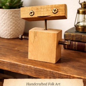 Könnte beinhalten: Eine handgefertigte Holzroboter-Skulptur mit einem rechteckigen Kopf und Körper, verbunden durch eine Metallstange. Das Gesicht des Roboters hat zwei Schrauben als Augen und ein geschnitztes Lächeln. Schrauben werden als Arme verwendet. Der Text auf dem Bild lautet "Wooden Robot".