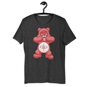 May include: Dark grey t-shirt with a red cartoon bear design. The bear has its tongue out and hands on its face, with a 666 symbol on its belly. The t-shirt is displayed on a black hanger.