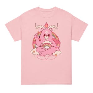 Peut inclure: T-shirt rose avec un motif graphique d'un ours en peluche rose avec des cornes de diable, un arc-en-ciel et un pentagramme.