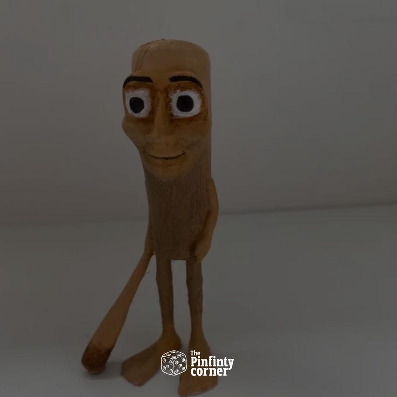 May include: A tan-colored, cartoonish figurine with a smiling face, large eyes, and a slender body. The figure has long, thin legs and arms, with one arm extended. The base of the figurine has the text "The Pinfinty corner".