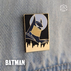 Pu&ograve; includere: Spilla rettangolare di Batman in smalto con bordo dorato. La spilla presenta il profilo di Batman su sfondo nero con una silhouette di skyline e una luna azzurra. La parola "BATMAN" &egrave; in basso.