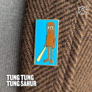 May include: A rectangular enamel pin featuring a cartoon character with a brown body, holding a yellow object against a blue background. The pin has a gold border and the text "TUNG TUNG TUNG SAHUR" at the bottom. The pin is attached to a brown tweed jacket.