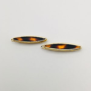 May include: Two gold hair clips with a tortoiseshell design. The clips are oval shaped and have a gold metal frame.