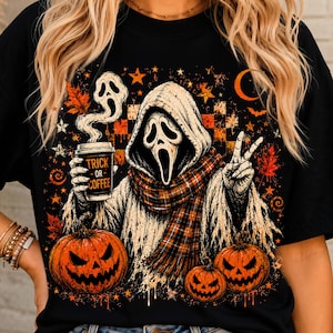 May include: A black t-shirt featuring a graphic of a hooded ghost figure wearing a plaid scarf, holding a coffee cup labeled "TRICK OR COFFEE" and making a peace sign. The design includes orange pumpkins, autumn leaves, stars, and a crescent moon.