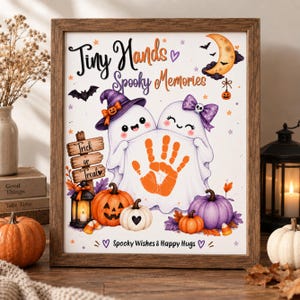 Peut inclure: Une impression encadrée d'Halloween montrant deux fantômes de dessin animé tenant un drap avec une empreinte de main orange au centre. Le texte indique Tiny Hands Spooky Memories, Trick or Treat, et Spooky Wishes & Happy Hugs, avec des citrouilles.