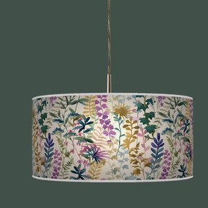 May include: A cylindrical pendant lamp with a floral design. The lampshade displays a watercolour pattern of diverse flowers and foliage in shades of purple, green, yellow, and blue against a cream backdrop. The lamp is suspended from a silver cord.