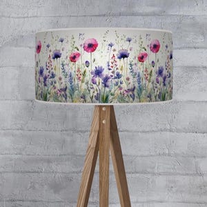 May include: A lampshade with a watercolour floral design featuring pink and purple flowers, green foliage, and a white background. The lampshade is mounted on a wooden tripod lamp base.