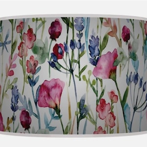 May include: A cylindrical lampshade with a watercolour floral design. The pattern features pink, red, and blue flowers with green stems and leaves against a white background. A home decor item.