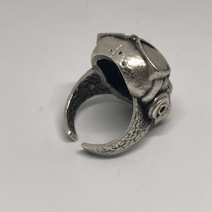 K&ouml;nnte beinhalten: Ein silberfarbener Ring mit einem einzigartigen Design. Der Ring hat eine detaillierte, strukturierte Oberfl&auml;che mit offenem Design. Das Design des Rings umfasst eine abgerundete Oberseite mit einem kreisf&ouml;rmigen Detail und eine schuppenartige Textur am Band.